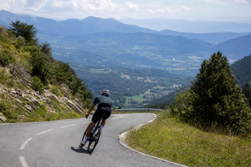 Road cyclist descending a winding Pyrenees pass above a green valley